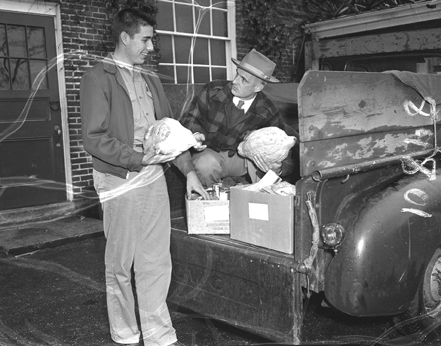 Principal Rutherford M. Drummond of Falmouth High School, right, tuned deliveryman yesterday to aid the Future Homemakers of the school in providing Thanksgiving baskets for the needy of the town. He is aided by Brian Farwell, a senior.