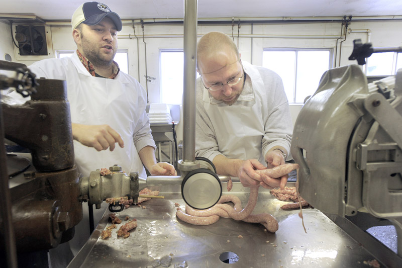 Reporter Ray Routhier, right, collects sausage from the linking machine under the watchful eyes of Marc Mailhot, whose family owns the sausage and meat pie factory in Lewiston.