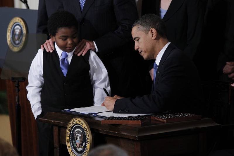 President Obama signs the health care reform bill Tuesday in the East Room of the White House as Marcellus Owens, 11, from Seattle, Wash., and government officials watch. Owens was later given one of the signing pens.