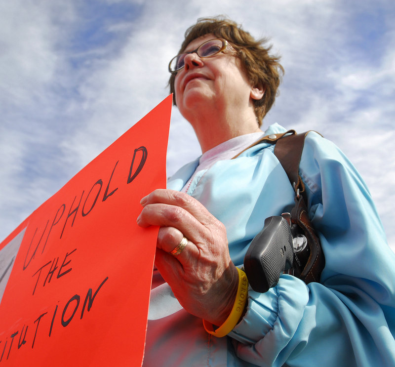 Mary Lou Bagley, 63, of Portland carries a .38-caliber Smith & Wesson and holds a sign reading "Uphold the Constitution" at Back Cove in Portland during an open-carry gathering Sunday.