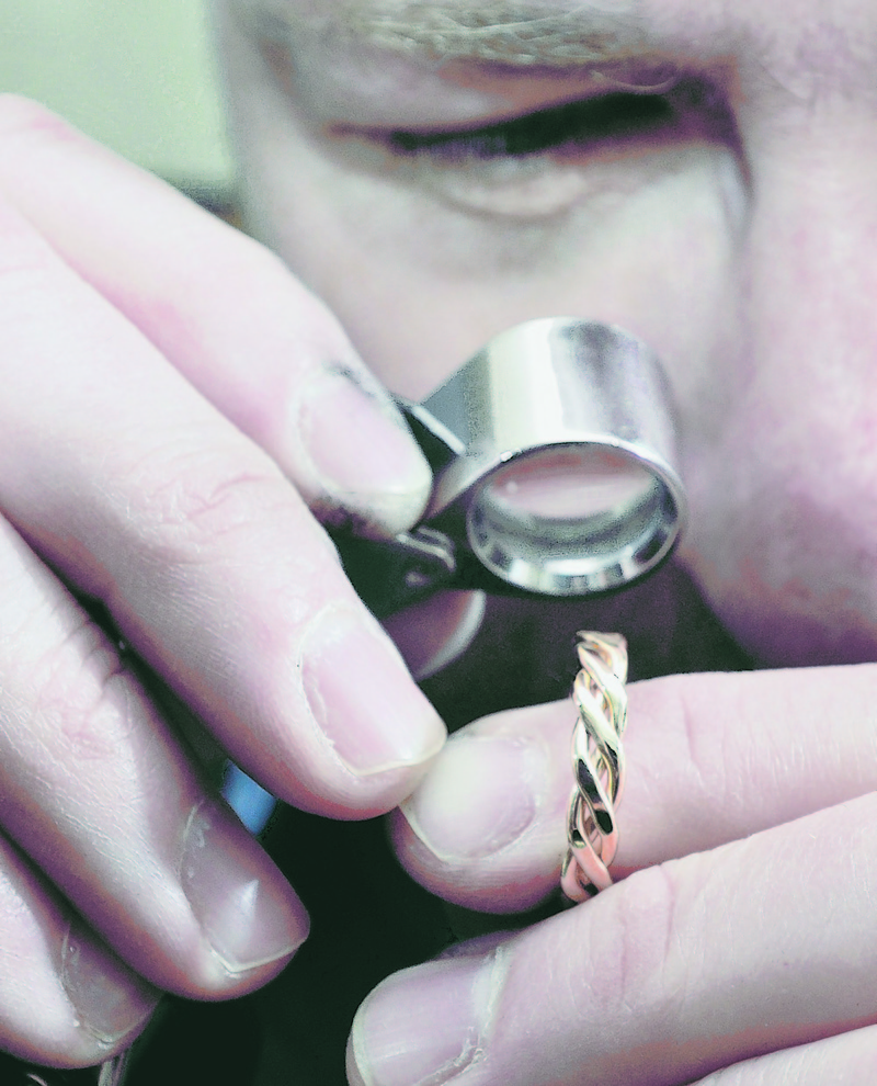 Deane Frank oversees the process of melting grains of gold to weld the ends of three gold wires together with a torch as Ray Routhier learns how to make a wedding band.