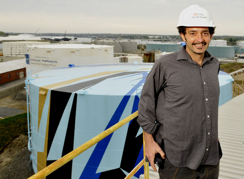 Artist Jaime Gili visits the Sprague Oil Tank farm in South Portland. The next tank to be painted is the tank on the left, in the background. It is being scraped and undercoated before the final design is rolled on by a crew with a paint company owned by Georgia Flanagan.