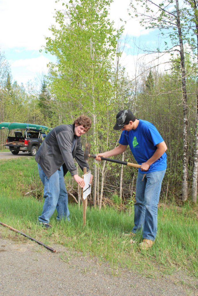 East Grand High School freshman Mitchell Bartlett holds a race sign while sophomore Andrew Gilman hammers it in on May 7, the day before the school’s multi-sport adventure race.