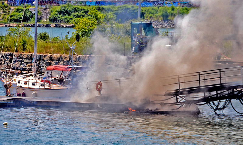 Portland firefighters battle a fire caused by a fuel line break at the Maine Yacht Center off Kensington Street in East Deering today. The fire started around 12:15 p.m., according to Mike Billingslea, who lives in the adjacent neighborhood. He said he heard several pops possibly from the gas line and then several more possibly from the diesel line. on the ramp that connects the floating slips to the pier