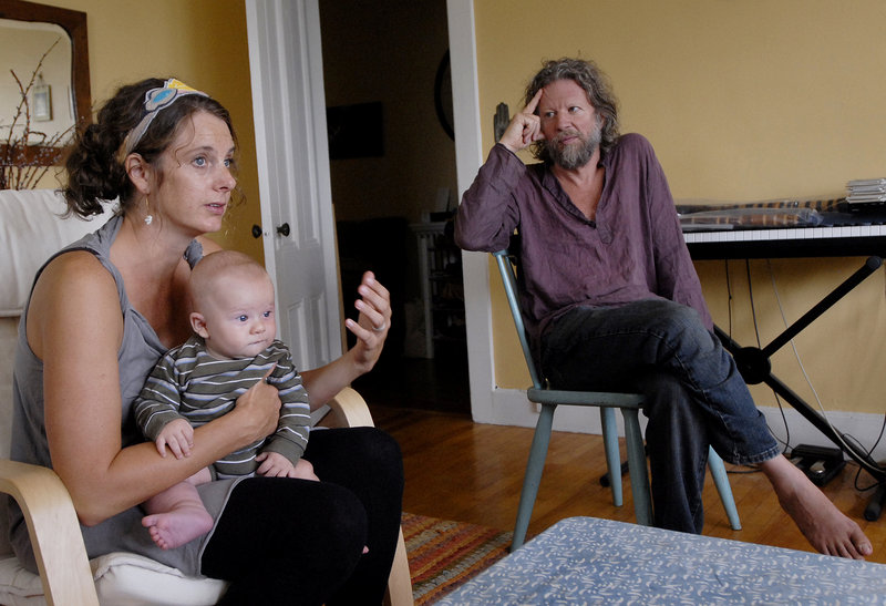 Lara Schneider shares her story while holding her son Julian in the family’s Portland apartment. At right is her husband, flutist Phil James, who is recovering from a stroke.