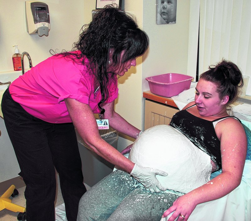 Katherine O'Connor loosens the casting material on Nicole Rocray's stomach. O'Conner is holding a belly-casting event in Biddeford on Thursday.