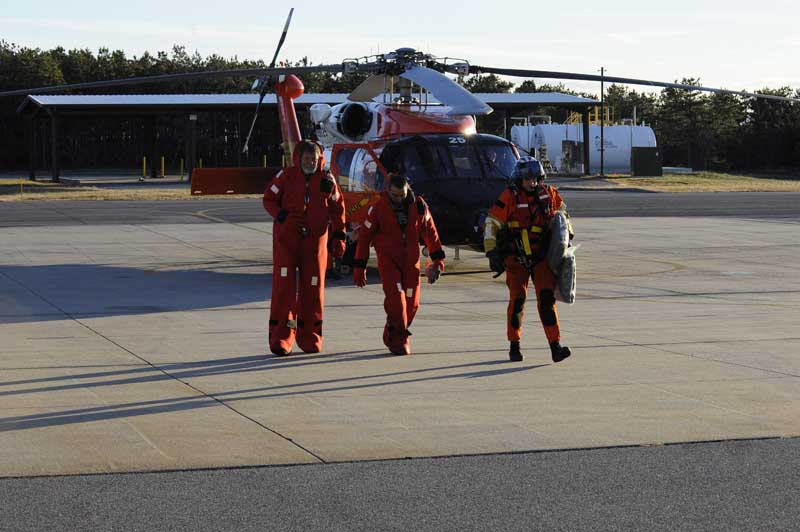 U.S. Coast Guard rescue swimmer Randall Rice escorts rescued mariners from a HH-60 Jay Hawk Rescue Helicopter at Air Station Cape Cod, Dec. 7, 2010. The mariners were rescued after the sailing vessel Raw Faith became disabled 100-miles