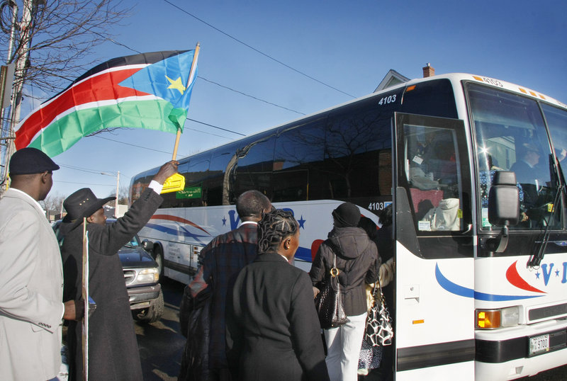 David Alana waves a Sudanese flag as Sudanese immigrants in Portland board a bus Sunday at The Root Cellar to travel to Boston to cast ballots in the country’s national referendum.