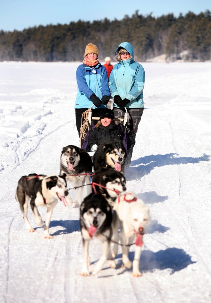 Shannon Bryan, sitting, rides in a dogsled during the 2010 Mushers Bowl Winter Carnival. Standing on the back of the sled is Gaetana Almeida, left, and musher Kate Kelly.