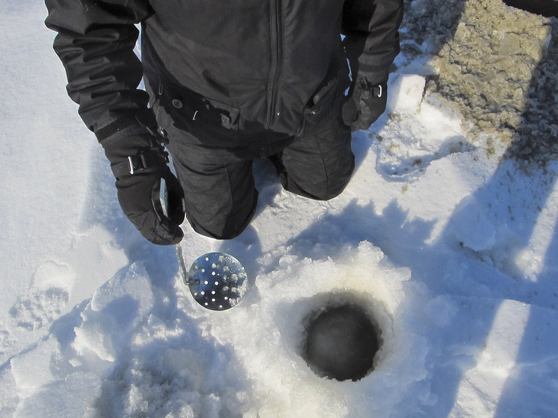 Reporter Shannon Bryan uses a large metal scoop to remove remaining slush from the hole after drilling.