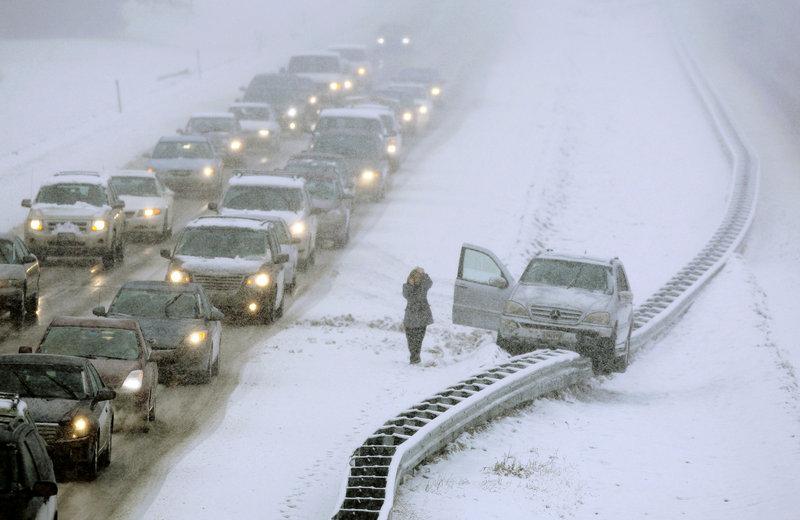 A woman uses a cell phone after exiting a vehicle that ended up atop a guardrail in the median of Interstate 295 in Cumberland during Friday’s storm. Portland received 9.4 inches of moisture-laden snow, with heavier accumulations inland.