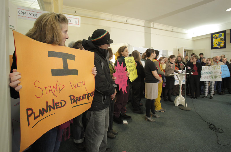 Lizzy Reinholt of Stratton, left, holds a sign during a news conference organized by the Maine Choice Coalition at the First Parish Church in Portland on Tuesday. More than 100 people attended to protest efforts to cut federal funds for family planning clinics.