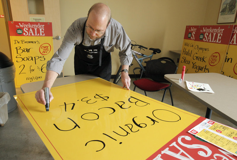 Ray Routhier works on a sign advertising organic bacon at Whole Foods Market in Portland. The large signs are hung in the windows of the store so passers-by can see them.