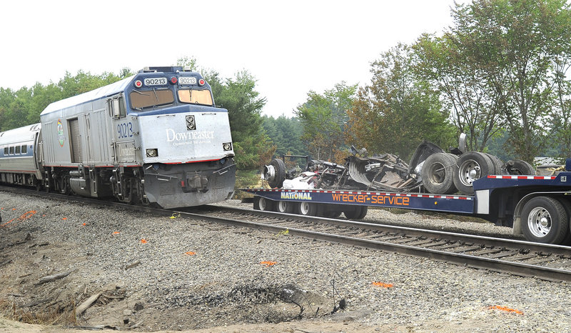 Amtrak’s Downeaster passenger train on Tuesday passes by a flatbed trailer that holds the remains of a 2009 Kenworth trash compactor truck that had been struck by a northbound train Monday along a Route 4 rail crossing in North Berwick.