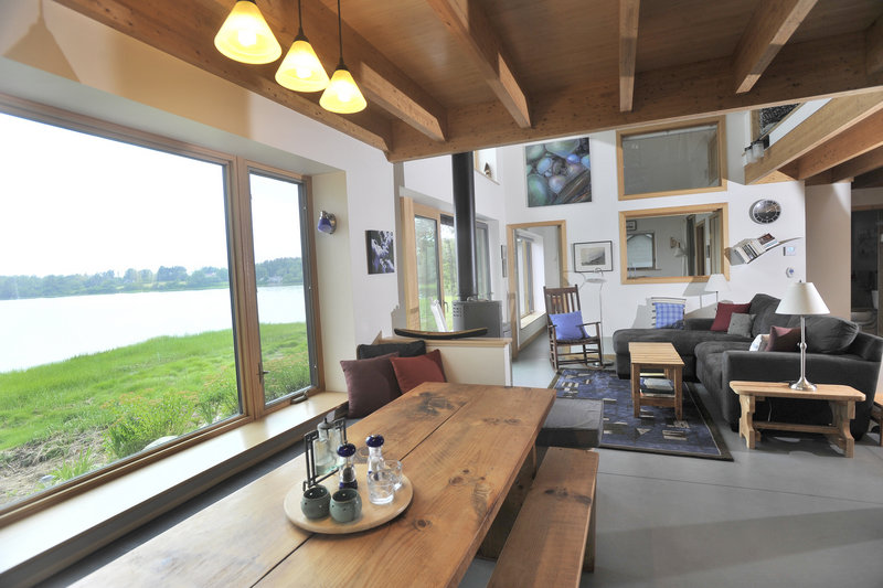 The living area is bathed in light from large windows overlooking the shore.