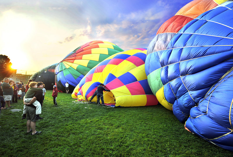 As the sun makes it way over the horizon, early-morning spectators watch hot air balloons being inflated by high-power fans at Railroad Park in Lewiston on Saturday. They will rise tall with blasts of hot air powered by propane burners.