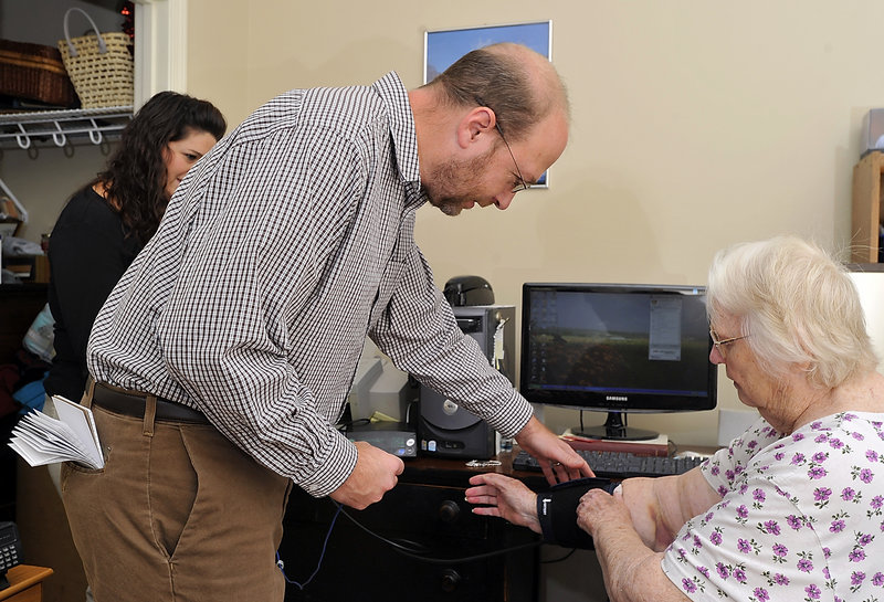 Ray Routhier helps Jeanette Holmes of Windham with her blood pressure cuff as nurse Christie Jordan, at left, supervises. Between visits, an automated system can track Holmes’ weight and vital signs.