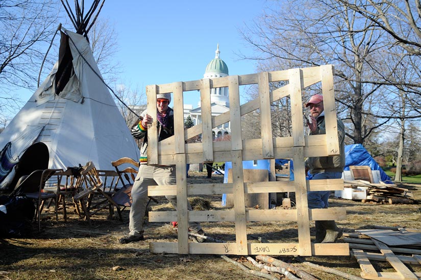 UNOCCUPIED: Occupy Augusta movement members Lew Kingsbury, right, and Nick Messier carry the platform for a tent out of Capitol Park in Augusta today after the group decided to break camp following a federal court ruling that directed the group to obtain a permit to remain in the park. Kingsbury said police advised Occupy Augusta to have all the structures removed by the end of business Thursday and the park cleaned up by Friday morning.