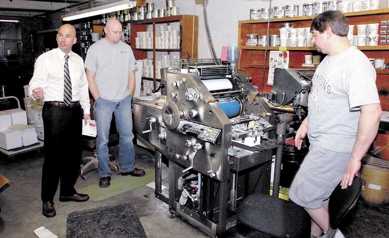 Jim Mitchell, left, co-owner of Atkins Printing Service in Waterville, speaks about the company as employees Randy Lovely, center, and Howard Dyer operate a press.