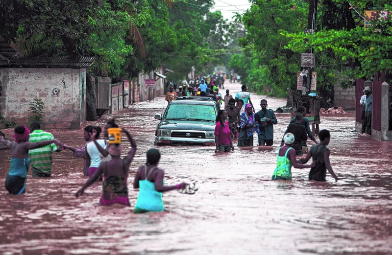 Above, Haitians wade through a street Saturday in Port-au-Prince in the wake of Tropical Storm Isaac. Below, Lowes employees Robert Tucker, right, and John Lucenti, left, load plywood for Terry King, back, and Ofelia Murphy on Saturday in Fort Walton Beach, Fla. The plywood will cover windows, with Isaac forecast to make landfall Tuesday in the Panhandle as a hurricane.