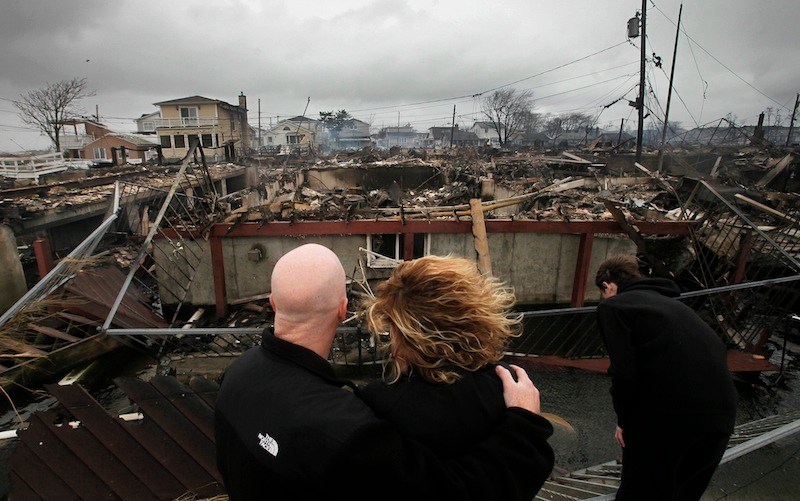 Robert Connolly, left, embraces his wife Laura as they survey the remains of the home owned by her parents that burned to the ground in the Breezy Point section of New York, Tuesday, Oct. 30, 2012. More than 50 homes were destroyed in the fire which swept through the oceanfront community during superstorm Sandy. At right is their son, Kyle. (AP Photo/Mark Lennihan)