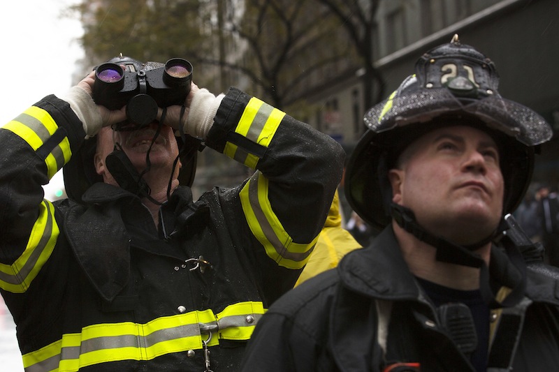 FDNY firefighters glare up at a damaged crane as it hangs over 57th Street after being torn from it's base by high winds, Monday, Oct. 29, 2012, in New York. Hurricane Sandy continued on its path Monday, as the storm forced the shutdown of mass transit, schools and financial markets, sending coastal residents fleeing, and threatening a dangerous mix of high winds and soaking rain. (AP Photo/John Minchillo)