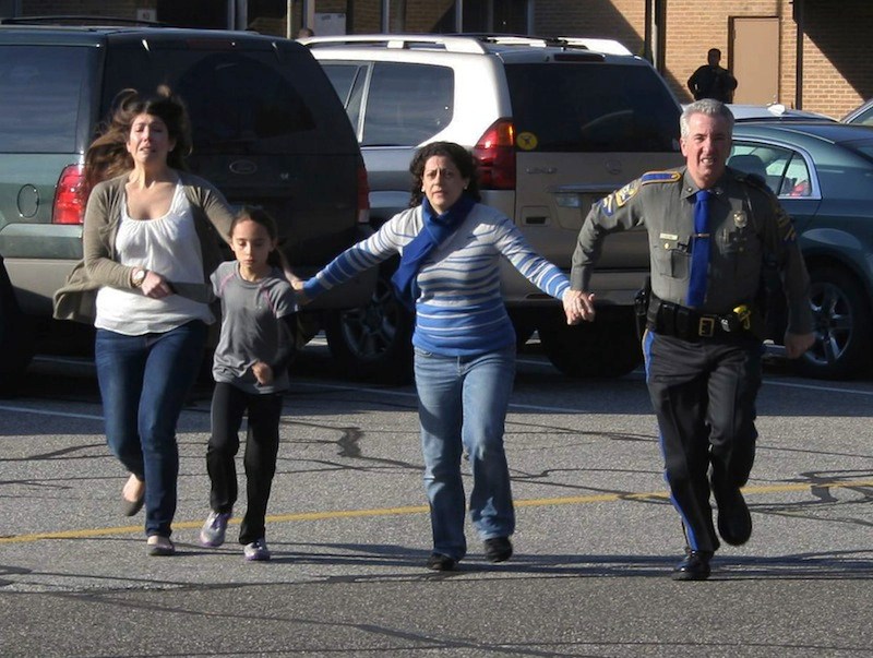 In this photo provided by the Newtown Bee, a police officer leads two women and a child from Sandy Hook Elementary School in Newtown, Conn., where a gunman opened fire, killing 26 people, including 20 children, Friday, Dec. 14, 2012. (AP Photo/Newtown Bee, Shannon Hicks)