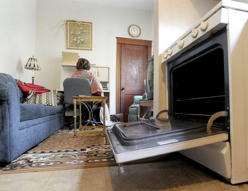 Fredence, a recent immigrant from Burundi, bundles up in blankets and uses heat from her oven to try to keep warm in her Portland apartment.