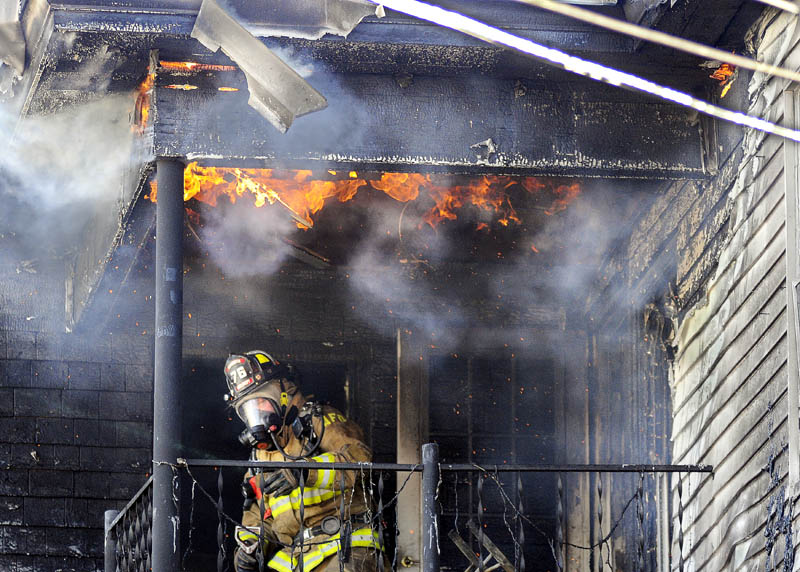 HOT TOP: An Augusta firefighter ducks beneath flames emerging from the third floor deck of an apartment building that burned Thursday, Jan. 10, 2013, on Sewall Street. Departments from several towns responded to the fire, which was reported around noon. The blaze caused severe damage to the building, located across from St. Michael School, and forced the 14 residents living there to seek shelter through the Red Cross and Salvation Army.