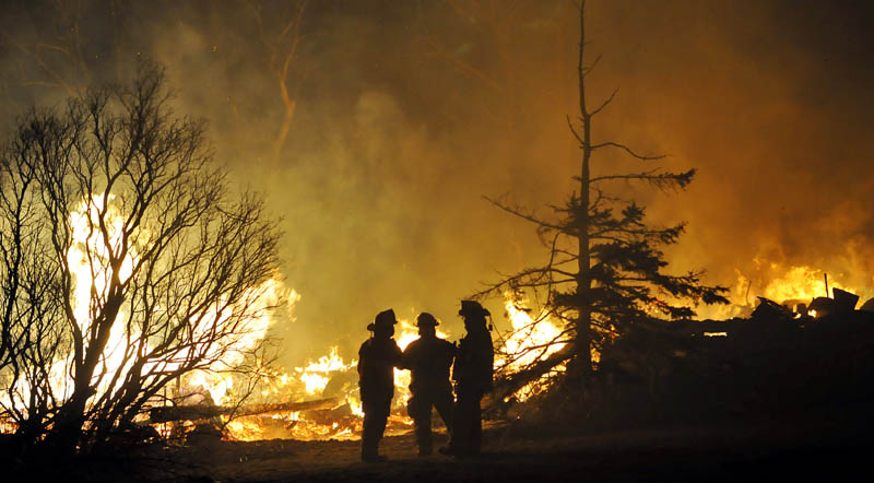 Firefighters confer next to the burning barn of a farmhouse that burned Thursday on the Crummett Mountain Road in Somerville. Firefighters were hampered in their efforts by severe cold temperatures.