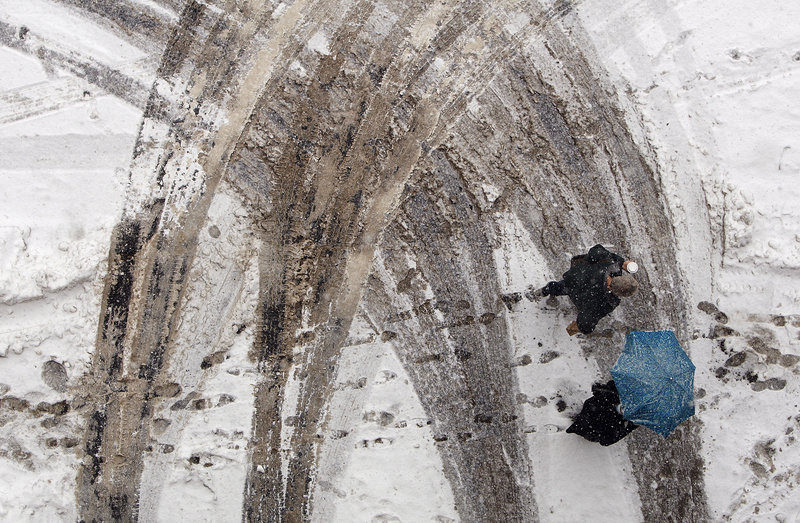 Two people walk along Free Street over tire tracks left in a wet snow that fell on Monday, February 11, 2013. Public Services employees have been working shifts of 16 hours on and eight hours off to try and clear the city's streets of last weekend's historic blizzard.
