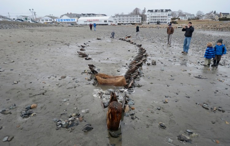 Beachgoers look over a ship's hull Monday that was uncovered at Short Sands Beach in York recently. The hull shows up from time to time when a storm washes away the sand. The hull was last seen following the Patriots Day storm in 2007.