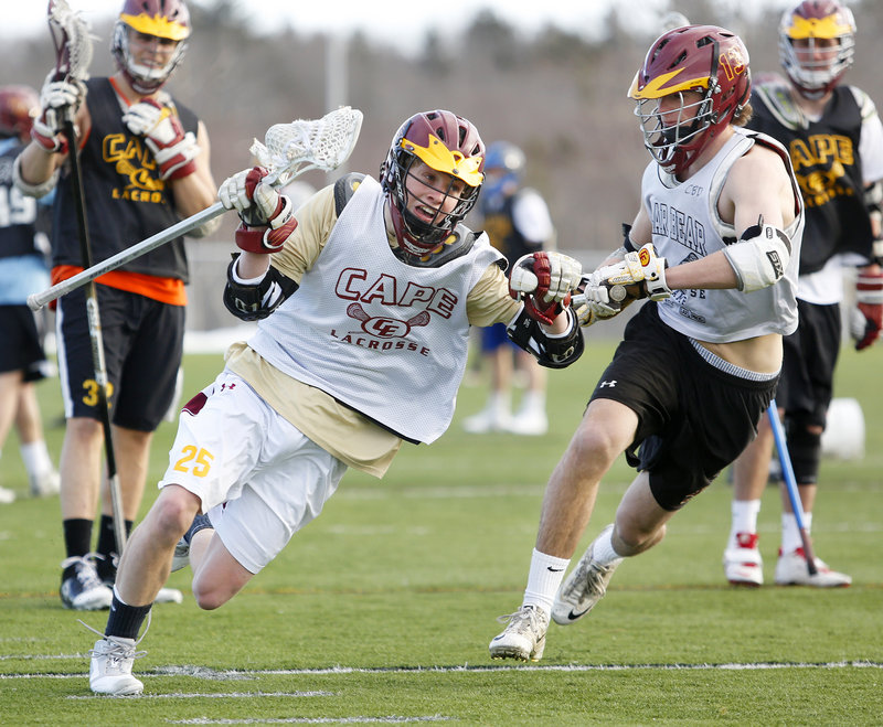 Photos by Derek Davis/Staff Photographer Cape Elizabeth junior Matt Fisher, center, works his way past junior defenseman Trevor Gale during the first lacrosse practice on the school’s artificial turf field Monday.