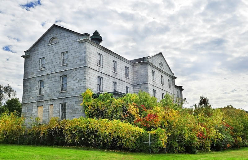 Staff photo by Joe Phelan The doors and windows of the the river front granite buildings of the Kennebec Arsenal have been boarded up for years.