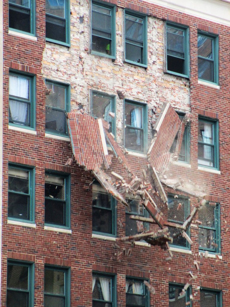 Bricks fall from the facade of 142 High St., the Congress Building, on Sunday, as workers inside the building try to shore up the structure.