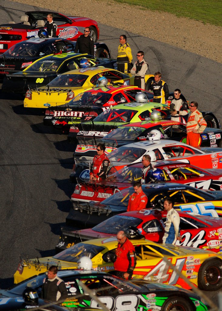 Drivers, with helmets propped atop their race cars, stand at attention just prior to the playing of the national anthem at the TD Bank 250 in Oxford.