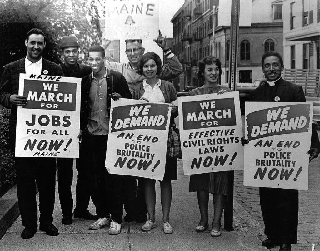 Tired but still enthusiastic, this delegation returned today from the civil rights demonstration in Washington. The "police brutality" placards did not apply, however, because capital law officers turned out gentlemanly and good-natured. Left to right are Gerald Talbot, Alfred Burris, Lawrence Graham, the Rev. Valton V. Morse, Miss Elizabeth Aldrich, Mrs. Joseph Robey, and the Rev. John C. Bruce. Published in the Aug. 29, 1963, Portland Evening Express.