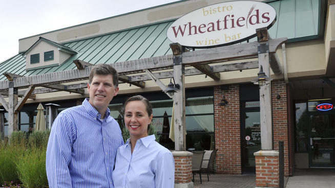 Bartender Sara Tucciarone, left, talks about a wine selection with hostess Hillary Len, right, and Wheatfields Restaurant owners Tim Holmes and his wife Colleen at the business in Clifton Park, N.Y. on Tuesday, Sept. 10, 2013. The Holmes were considering opening a third business but decided against it. One factor was the risk in expanding their staff beyond 50 full-time employees and having to provide federally mandated health coverage in 2014. Despite knowing the penalty provisions for noncompliance have been postponed one year, the couple said their margins are thin and the requirements and costs of the health care law are not yet clear.