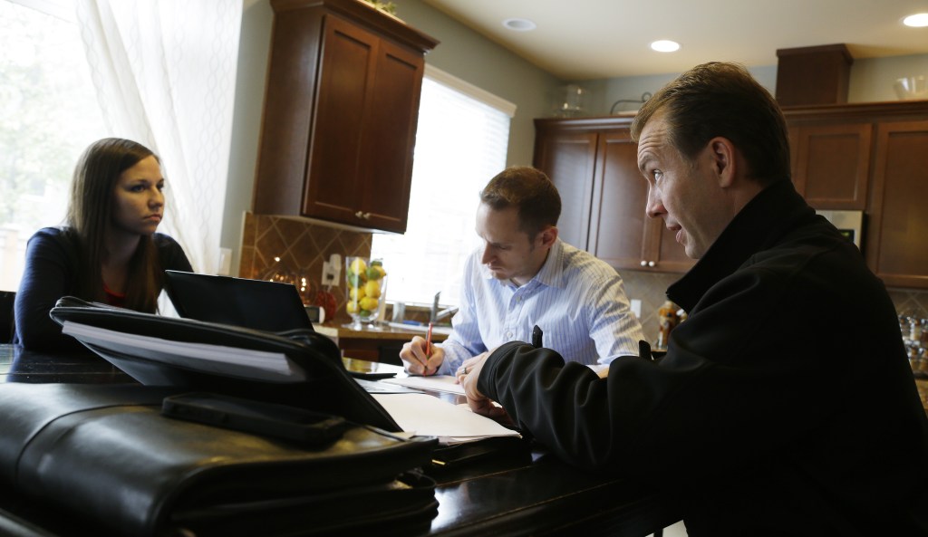 The Associated Press Insurance broker Jeff Lindstrom, right, meets with Brandi and Darren Litchfield to discuss health insurance plan options, at their home in the Seattle suburb of Bothell, Wash. Darren works for a startup company that doesn’t yet offer an employee insurance plan, so they invited Lindstrom to outline the options of different healthcare plans that he offers as a broker.