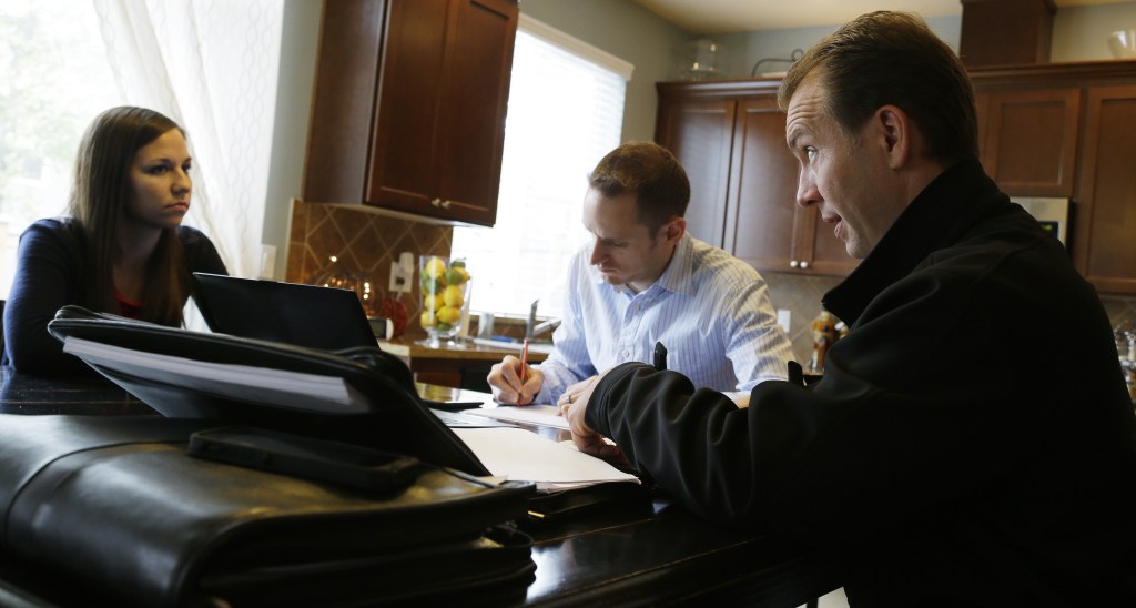 Insurance broker Jeff Lindstrom, right, meets with Brandi and Darren Litchfield to discuss health insurance options at their home in the Seattle suburb of Bothell, Wash. Darren Litchfield works for a startup company that doesn’t yet offer an employee insurance plan, so the couple invited Lindstrom to outline the options of different plans that he offers.