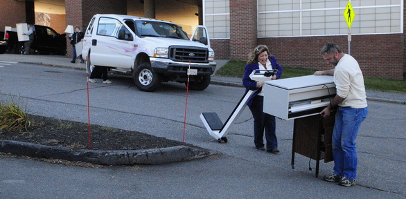 Deb Poulin reacts as a cabinet Lou Berthell is pushing catches in the pavement and almost tips over outside the sale of items from the former MaineGeneral Medical Center.