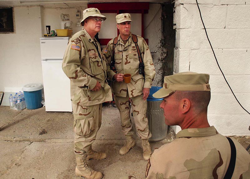 Staff photo by Gregory Rec -- Thursday, April 22, 2004 -- Major John Nelson, right, talks with Staff Sgt. Patrick Labrie in front of the medical center for the 133rd Engineer Battalion at Camp Marez in Mosul, Iraq. Nelson, a physician's assistant from Bangor, leads the 133rd's medical staff and is known around camp as "Doc Nelson." Labrie is a medic at the station. In the foreground, Spc. James Martinez waits for treatment. Iraq