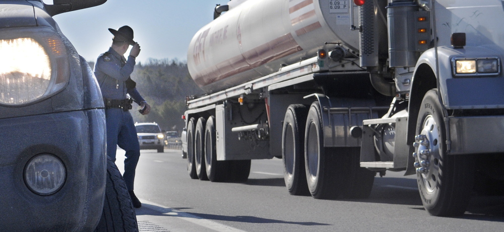 Maine State Trooper Chris Rogers holds on to his Stetson Thursday as a tractor-trailer passes him during a traffic stop in West Gardiner. Several State Police cruisers have been struck while parked at accidents this year, compelling police to remind drivers that they must slow down and pull over when approaching emergency vehicles.