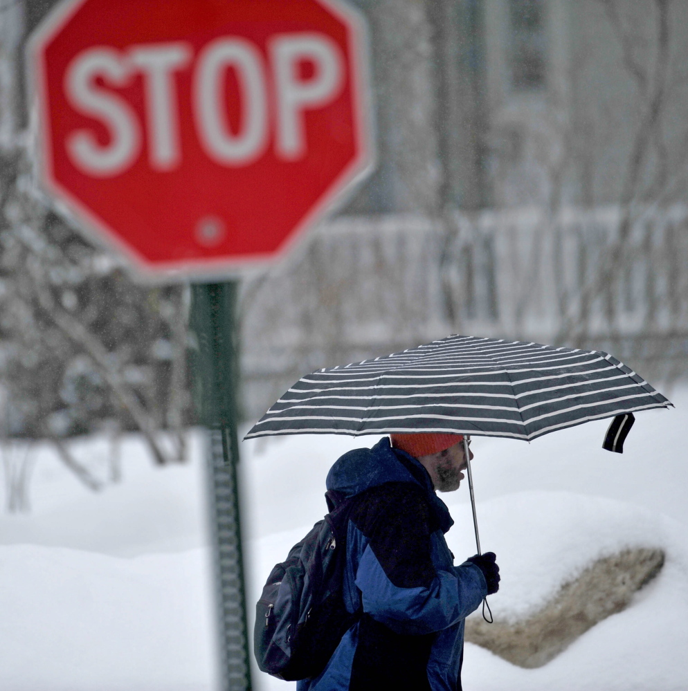 SPRING STORM: John Ervim walks along Gilman Street as rain falls in Waterville on Thursday.