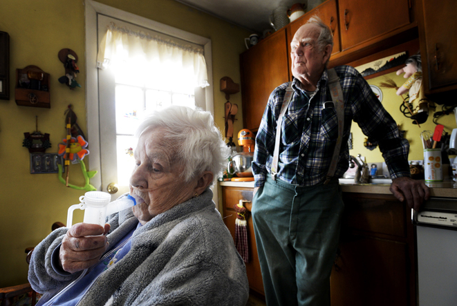 Corinne Murray takes her twice-daily mist treatment at her Cape Elizabeth home. A team of medical professionals help her husband, Arnold (background), with his wife's overall care as part of a pilot program aimed at keeping patients engaged in their own care, and out of hospitals.