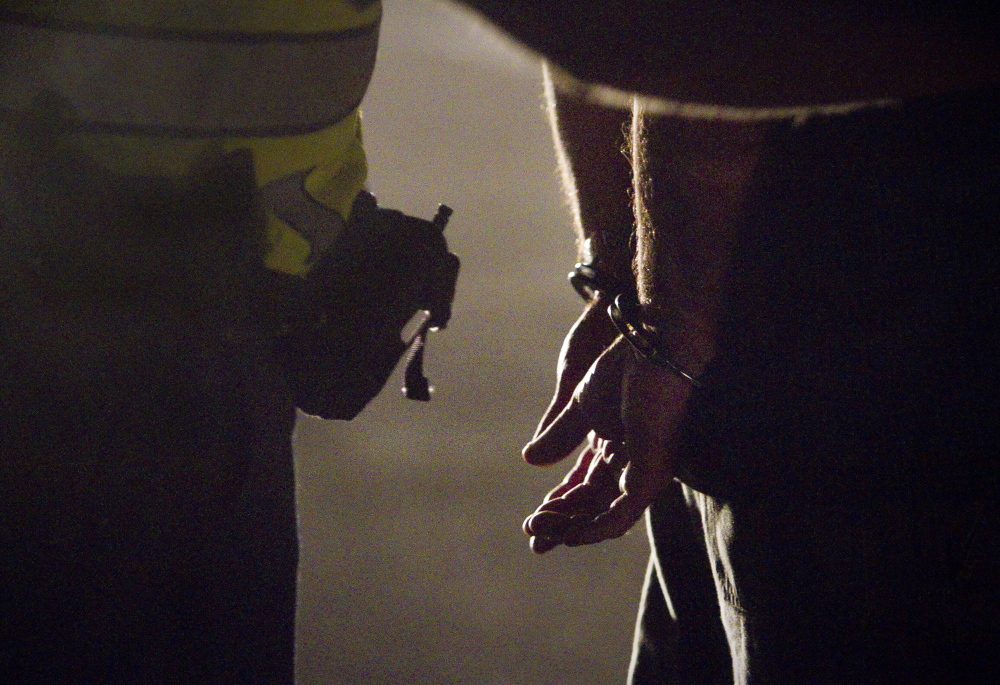 Cumberland police Officer Ryan Martin cuffs a motorist suspected of drunken driving before bringing him to the Brunswick police station for a breath test. Martin was part of a regional team doing sobriety checks on Route 1 last August.