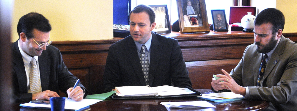 House Majority Leader Seth Berry, D-Bowdoinham, left, signs a document Thursday while huddling with House Speaker Mark Eves, D-North Berwick, and Assistant Leader Jeff McCabe, D-Skowhegan, ahead of the legislative session at the State House in Augusta.