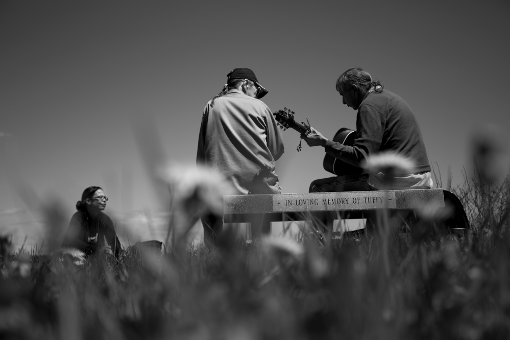 Melissa Altvater, left, and her father, Dave Homan, center, listen as tribal elder Allen Sockabasin plays guitar near the water at Pleasant Point in Washington County. Sockabasin is a longtime champion of the Passamaquoddy language, “the key to open the lock of independence for native people.”