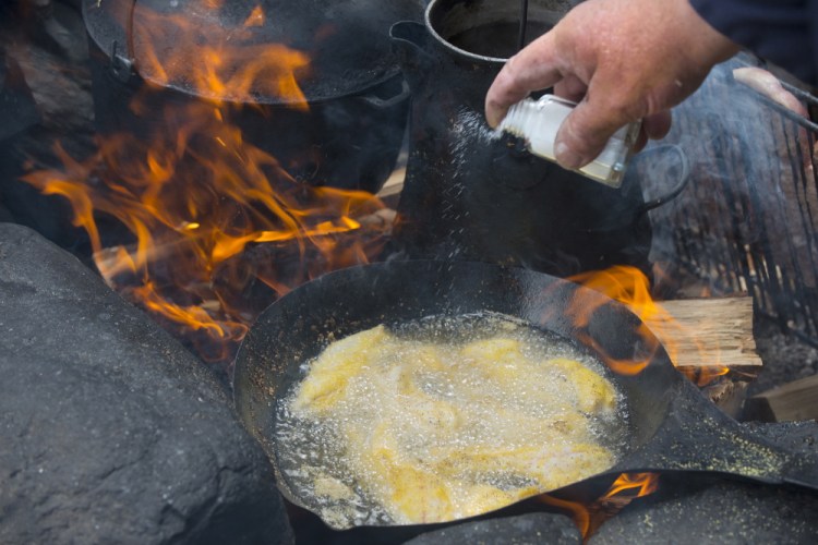 Guide Lance Wheaton adds a dash of salt to fish filets frying over a wood fire.