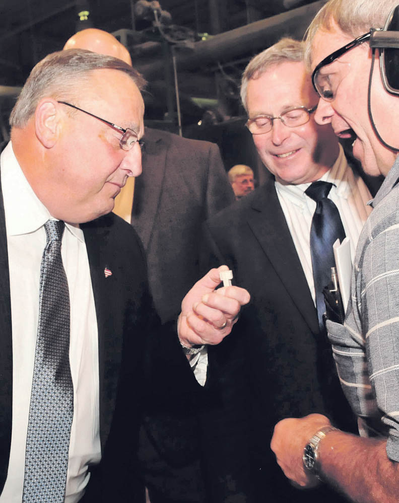 Gov. Paul LePage, left, examines a Lincoln Log piece that was milled at Pride Manufacturing in Burnham on Wednesday, along with Maine Commissioner of Agriculture Walt Whitcomb and Randy Dickers of Pride. 